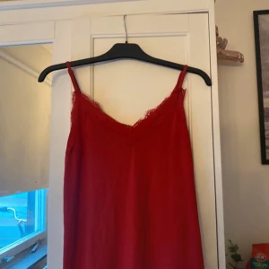 Röd spetsklänning med smala axelband - Säljer en röd klänning med smala axelband och fina spetsdetaljer upptill. Klänningen har en enkel och elegant design, perfekt för dig som gillar en feminin stil. Passar lika bra till sommarens alla tillfällen.