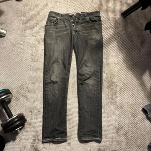 Grå jeansbyxor från Jacob Cohën - Säljer ett par grå jeansbyxor från Jacob Cohën  med raka/slim ben och slitna detaljer vid benslut och fickor. Byxorna har knappar i gylfen. I helhet ganska slitna byxor som lätt går att laga, säljes därav till billigt pris.