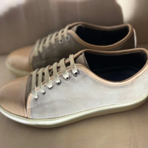 Beige LANVIN sneakers - Snygga beige sneakers från Lanvin med ovandel i mocka och detaljer i skinn. Skorna har rund tå, snörning och vit sula. Perfekta för en stilren och avslappnad look. Storlek 42 (passar 41) okej skick. Hör av dig vid minsta fundering!! Ingen box eller dust ag ingår. ♟️‼️PRIS KAN DISKUTERAS‼️‼️