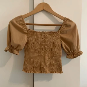 Beige ribbad topp med puffärmar - Säljer en söt beige topp med puffiga kortärmar och ribbad design. Aldrig använd. Köpt utomlands. I storlek M men passar XXS-M då den sitter ganska tight. Säljer även i svart.