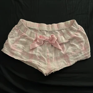 Rosa och vita shorts med rosett - Söta och bekväma shorts i rosa och vitt med en charmig rosett framtill. Perfekta för en avslappnad dag hemma eller en somrig utflykt. 