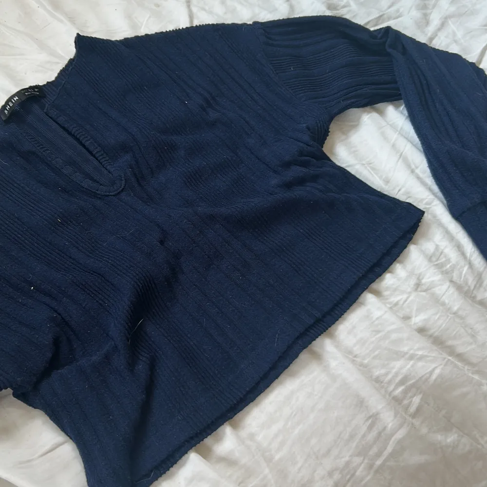 Säljer en mörkblå croppad tröja från NA-KD med ribbad struktur. Tröjan har långa ärmar och en liten v-ringning vid halsen. Perfekt till jeans eller kjol för en avslappnad look.. Neuletakit & Villapaidat.