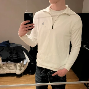 Vit half-zip tröja med dragkedja från Ralph Lauren - Säljer en stilren vit långärmad tröja från Ralph Lauren med halv dragkedja och broderad logga på bröstet. Perfekt för en clean och klassisk look. Passar till jeans eller chinos.