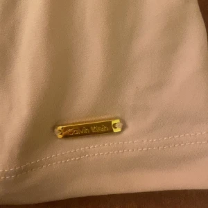 Beige linne från Calvin Klein - Elegant beige linne från Calvin Klein med en stilren design. Linnen har en vacker drapering framtill som ger en fin siluett. Perfekt för en stilfull look.