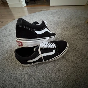 Svarta och vita Vans Old Skool sneakers - Klassiska Vans Old Skool sneakers i svart med vit sidorand och vita snören. Skorna har låg profil, vit sula och tydliga kontrastsömmar. Perfekta för en avslappnad och stilren look. De är knappt använda och vid köp rengörs de självklart innan då sulan blivit lite smutsig, (inget permanent). 