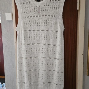 Vit stickad klänning - Säljer en vit stickad klänning med ett vackert hålmönster. Klänningen är ärmlös och har en rak passform som ger en avslappnad look. Perfekt för lager-på-lager-stil eller sommarens varma dagar.