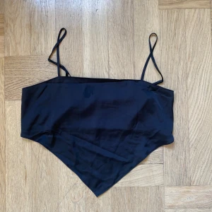 Svart croppad linnetopp med smala axelband - Säljer en svart croppad linnetopp med smala axelband och spetsig nederkant. Toppen har en slät framsida och smockad rygg för extra komfort. Perfekt till sommaren och enkel att matcha med olika outfits.