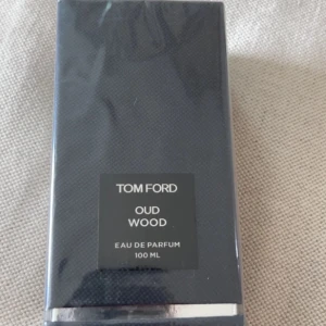 Tom Ford Oud Wood Eau de Parfum 100 ml - Exklusiv parfym från Tom Ford, Oud Wood Eau de Parfum i 100 ml förpackning. Kommer i en elegant, mörkgrå kartong med stilren design och silverdetaljer. En lyxig doft med träiga och orientaliska inslag.