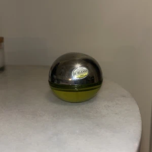 Be Delicious parfym från DKNY - Säljer en ikonisk Be Delicious parfym från DKNY. Flaskan är rund och formad som ett äpple med en metallisk silverfärgad topp och grön botten. Parfymen har en fräsch och fruktig doftprofil som är lätt att känna igen.