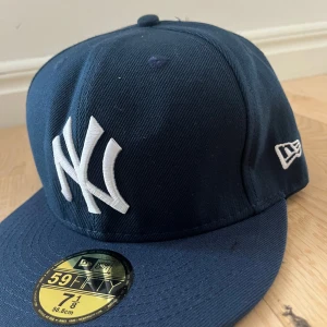 Mörkblå New Era 59FIFTY keps NY Yankees - Säljer en mörkblå New Era 59FIFTY keps med NY Yankees-logga broderad framtill i vitt. Klassisk rak skärm och New Era-logga på sidan. Kepsen är i storlek 7 1/8 (56,8 cm).