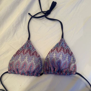 Mönstrad trekantsbikini med knyt - Säljer en trekantsbikini med färgglatt mönster i blått, rött och vitt. Bikinin har svarta knytband i nacken och ryggen, vilket gör den justerbar. Perfekt för sommardagar på stranden eller vid poolen.