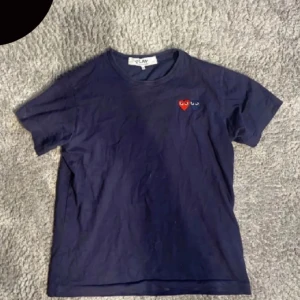 Cdg t-shirt - Säljer en mörkblå t-shirt från Comme des Garçons med två broderade hjärtan på bröstet. T-shirten har en klassisk passform och korta ärmar. Perfekt för en stilren look. Pris kan diskuteras vid snabbt köp.