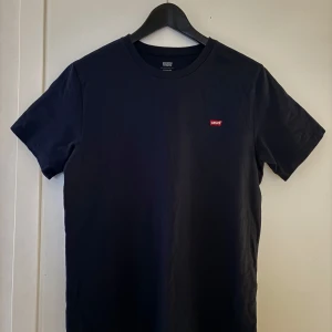 Mörkblå t-shirt från Levi's - Snygg mörkblå t-shirt från Levi’s med en liten röd Levi’s logga på bröstet. Perfekt för en stilren och enkel look. Gjord i mjukt bomullsmaterial för extra komfort. Köpte för 269kr. Endast använd 1 gång, säljer för att den inte satt bra på mig. Om du har frågor osv, bara o skriva!👊