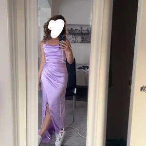 Ljuslila klänning - Säljer en elegant ljuslila klänning med slits framtill. Klänningen har en smickrande passform och är perfekt för speciella tillfällen. Materialet ger en fin glans och faller vackert. Använd en gång på niornas bal.
