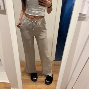 Beige linnebyxor med dragsko - Snygga beige linnebyxor med dragsko i midjan för en bekväm passform. Byxorna har en loose fit och är perfekta för en avslappnad stil. De är sprättade nertill för att de sulle bli lite längre och passar bra till både sneakers och sandaler.