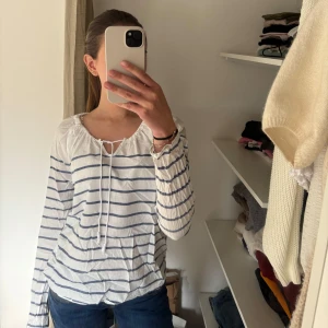 Vit och blå randig blus - Säljer en vit blus med blå ränder och knytband vid halsen. Blusen har långa ärmar och en avslappnad passform, perfekt för en stilren look. Passar bra till jeans eller kjol för en casual stil. Jag säljer den då den tyvärr börjar bli för liten för mig😊Står storlek M, men skulle säga att den passar S/XS också