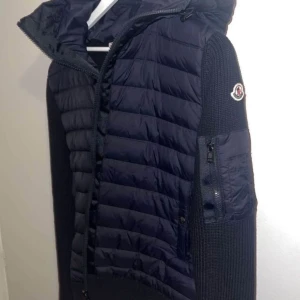 Moncler cardigan herr - Säljer en mörkblå Moncler-jacka med vadderad framsida och stickade ärmar. Jackan har huva, dragkedja och en ficka med dragkedja på ärmen. Perfekt för kyliga dagar och snygg till streetwear, moncler cardigan herr äkta, säljer min cardigan jag inte använder, storlek S