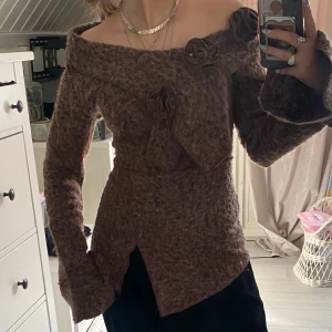Brun offshoulder tröja - Säljer en unik brun offshoulder tröja med blommiga detaljer och knytning framtill. Den är helt oanvänd och endast testad, det är inte riktigt min smak!! Passar för 36/34