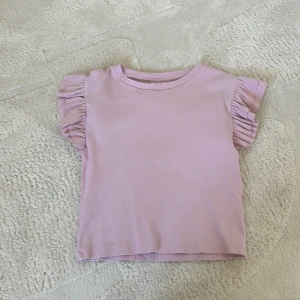 Ljuslila topp med volangärmar - Söt ljuslila topp med korta volangärmar. Perfekt för en somrig look. Tillverkad i ett mjukt material som känns skönt mot huden.