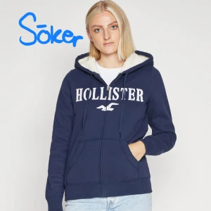 SÖKER Mörkblå hoodiejacka från Hollister - Söker denna hoodie helst storlek S-L. Mysig mörkblå hoodiejacka från Hollister med vit logga framtill, dragkedja och snörning i huvan. Fodrad med vit teddyfleece på insidan av huvan och har kängurufickor. Perfekt för chill dagar och enkel att matcha.