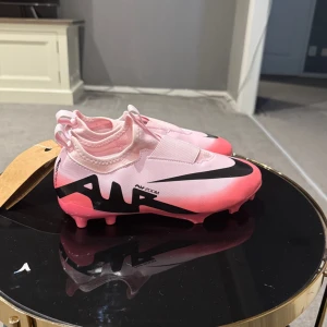 Nike Air Zoom rosa fotbollsskor - Säljer ett par Nike Air Zoom Mercurial fotbollsskor i en snygg ljusrosa färg med svarta detaljer och stor Swoosh-logga. Skorna har elastiskt band över vristen och är gjorda i syntetmaterial för bästa passform på planen. Perfekta för dig som vill sticka ut på matchen!