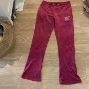 Juicy conture  - Mysiga mörkrosa / lila mjukisbyxor  med snörning i midjan och två bakfickor. På ena benet finns en glittrig strassdetalj i form av ett JC. Perfekta för alla dagar