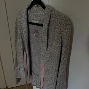 Mönstrad cardigan jacka Odd Molly - Cardigan jacka från Odd Molly i ljusgrått och rosa med diskret mönster. Jackan har knytband i midjan och broderad logga på insidan. Mjuk och skön, perfekt för lager-på-lager-stil. Långärmad och i stickad bomullsblandning. Sitter som en storlek S