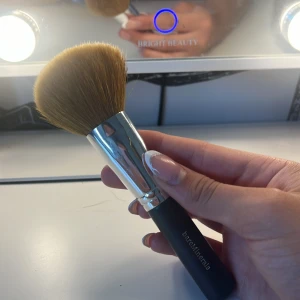 Stor sminkborste från bareMinerals - En fluffig och mjuk sminkborste från bareMinerals med svart handtag och silverfärgad metall vid borsthuvudet. Borsten är tät och rundad, perfekt för att applicera puder, bronzer eller rouge. Handtaget är matt och greppvänligt.