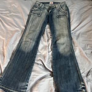 Bootcut jeans från Colours of the World - Snygga bootcut jeans från Colours of the World i tvättad blå denim. Jeansen har stora fickor fram och bak, markerade sömmar och en klassisk bootcut passform. Perfekta för dig som gillar retrovibbar och vill ha ett par jeans med lite extra attityd.