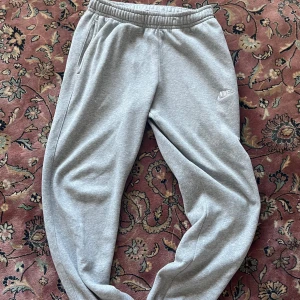 Nike Grå mjukisbyxor  - Snygga grå mjukisbyxor från Nike med elastisk midja och muddar vid bensluten. Byxorna har sidofickor och en liten vit Nike-logga på låret. Perfekta för chill eller träning, riktigt sköna och stilrena. Inga defekter, avslappnade mjukisbyxor. Storlek L 