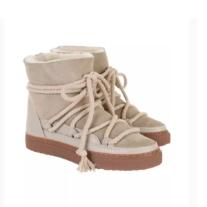 Beige boots från Inuikii med snörning - Snygga beige boots från Inuikii med grov snörning runt hela skon och brun sula. Utsidan är i mocka och skinn, insidan är fodrad med mjuk päls för extra värme. Perfekta för kalla dagar och ger en cool vinterlook. Nyköpta förra året så väldigt fint skick fortfarande 