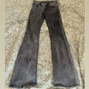 Low waist bootcut jeans - Snygga grå bootcut jeans från SHEIN i storlek XS. Jeansen har en tvättad look, klassiska fem fickor och en liten sliten detalj på ena benet. Tillverkade i bomull, polyester och elastan för en bekväm passform.