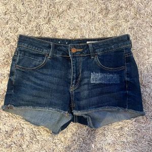 Mörkblå jeansshorts  - Snygga mörkblå jeansshorts med fransig kant och fyra fickor. Shortsen har en patchad detalj framtill och kontrastsömmar. Inge defekter. ❣️