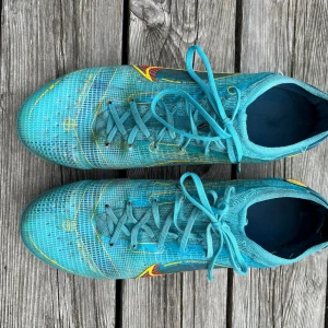 Nike Mercurial Vapor fotbollsskor blå - Säljer ett par Nike Mercurial Vapor fotbollsskor i blått med gula och röda detaljer. Skorna har snörning, låg profil och mönstrad ovandel i syntetmaterial. Perfekta för dig som vill sticka ut på planen med stilrena och sportiga skor.