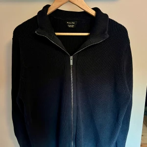 Svart ribbad kofta från Massimo Dutti - Säljer en svart ribbstickad kofta från Massimo Dutti i extrafin bomull. Koftan har hög krage och hel dragkedja framtill, perfekt för lager-på-lager. Stilren och enkel design som funkar till många outfits.