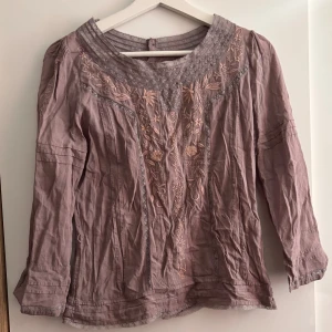 Ljuslila Blus - Superfin ljuslila blus från Birger et Mikkelsen med broderade blommor framtill och spetsdetaljer vid halsringningen. Blusen har långa ärmar och är gjord i ett mjukt bomullstyg. Använd ett par gånger men den är bara skrynklig inte sliten!