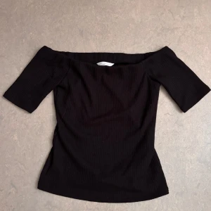 Svart Ribbad Topp - Snygg svart ribbad topp från H&M med offshoulder-modell och korta ärmar. Toppen har en ganska tight passform, storlek M. Aldrig använd!