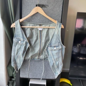 Jeansväst från Weekday, ljusblå - Knappt använd! Säljer en ljusblå jeansväst från Weekday i storlek 38. Västen har två bröstfickor med knappar, råa kanter och snörning framtill. Croppad modell med klassiska jeanssömmar och avslappnad passform.