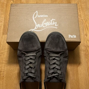 Grå Christian Louboutin Skor - Snygga sneakers från Christian Louboutin i mörkgrå mocka med klassisk röd sula. Skorna är i storlek 43 men passar 42. Skorna har rund tå, grå snören och diskreta ventilationshål på sidan. Lite slitna på den röda sulan därför lite billigare. Passar till det mesta. Skick 8/10. Lämnar skorna så fort den som köper köper dem om inte jag är borta.