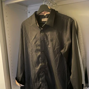 Svart Burberry skjorta - Snygg svart skjorta från Burberry med klassisk broderad logga på bröstet. Skjortan har långa ärmar, knappar framtill och ikoniskt rutigt tyg på insidan av manschetterna och kragen. Tillverkad i ett fint material som känns lyxigt och stilrent. Storlek large, använd 2 gånger, inga defekter 