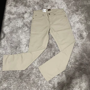 Beige Lee Daren Zip Fly Regular Straight - Snygga beige byxor från Lee, modell Daren Zip Fly Regular Straight. Klassisk femficksdesign, rak passform och dragkedjegylf. Tillverkade i mjuk bomull med en stilren look som passar till det mesta. Perfekta för dig som gillar enkel och clean stil.