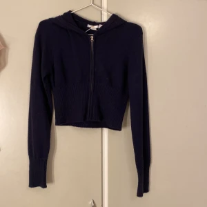 Mörkblå croppad stickad hoodie - Mörkblå croppad stickad hoodie med dragkedja framtill och huva. Endast använd ca 2 gånger 