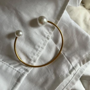 Guldfärgat armband med pärlor - Super fin ”bangle” från Timi of sweden med två pärlor i olika storlekar, armbandet är enbart i en storlek. Så lätt att matcha till allt och så himla fin!❤️ den är i stainless steal🥰💞