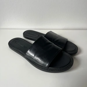 Svarta sandaler från Zara  - Stilrena svarta sandaler från Zara med bred rem över foten och platt sula. Använda enstaka tillfälle, mycket fint skick!