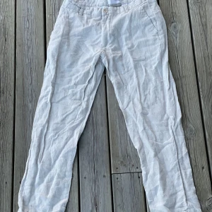 Beiga linnebyxor från Selected Homme - Snygga och luftiga beiga linnebyxor från Selected Homme. Byxorna har raka ben, sidfickor och hällor för bälte. Perfekta för varma dagar när du vill ha en chill och stilren look.
