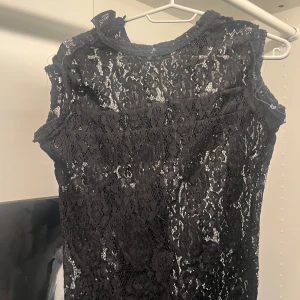 Svart spetsblus från Gina Tricot - Snygg svart blus i spets från Gina Tricot. Ärmlös modell med rund halsringning och transparent spetsmönster som ger en cool och elegant vibe. Perfekt att styla med jeans eller kjol för en trendig look.