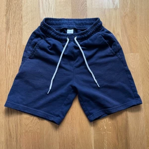 Mörkblå shorts från Lindex med snörning - Mörkblå mjuka shorts från Lindex med elastisk midja och vit snörning framtill. Snörena är för design och går av om man drar i dom. Shortsen har två sidofickor och är tillverkade i bomull, perfekta för chill dagar eller träning. Klassisk och enkel design som är lätt att matcha.