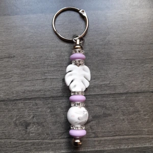 Nyckelring med lila och vita pärlor - Handgjord nyckelring med silikonpärlor i lila och vitt. Silverfärgade detaljer och glittrande mellanringar ger extra stil. Perfekt accessoar för att piffa upp dina nycklar.