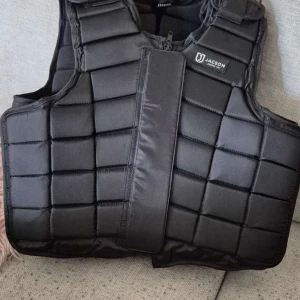 Svart skyddsväst från Jacson Junior - Säljer en svart, quiltad skyddsväst från Jacson i storlek Junior 14 år. Västen har rutmönstrad vaddering, dragkedja framtill och extra kardborre för säker passform. Perfekt för dig som rider och vill ha extra skydd.
