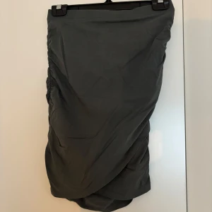 Mörkgrön omlottkjol med drapering - Snygg mörkgrön omlottkjol med draperad effekt på sidan. Kjolen har en cool, asymmetrisk form och är perfekt för dig som gillar stilrena plagg med en twist. Materialet känns mjukt och lätt, och kjolen har en normal passform.